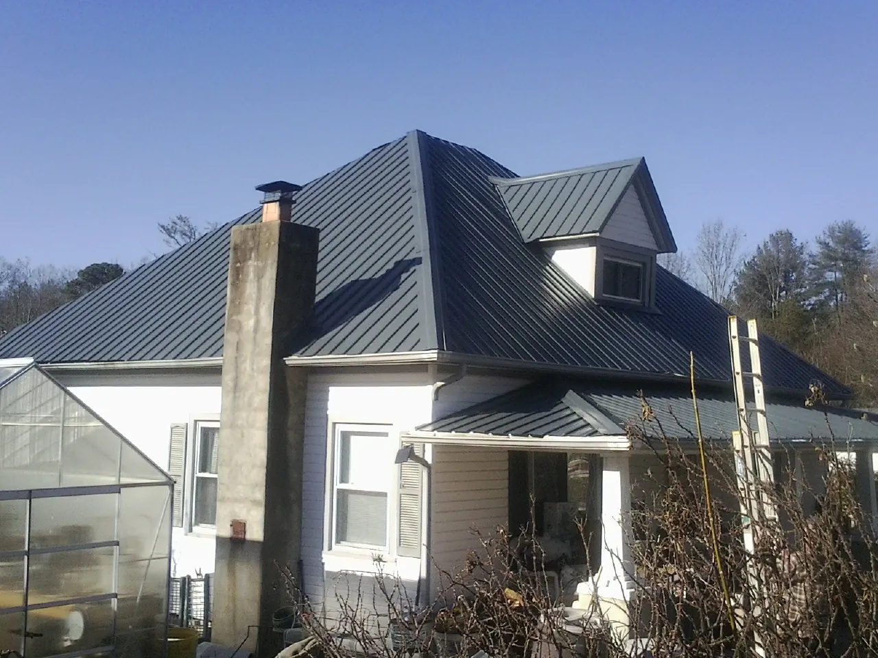 Dark blue standing seam metal roof on a white farmhouse with dormer — Slate & Tile Roof Repair by Roofing Brothers in Bostwick
