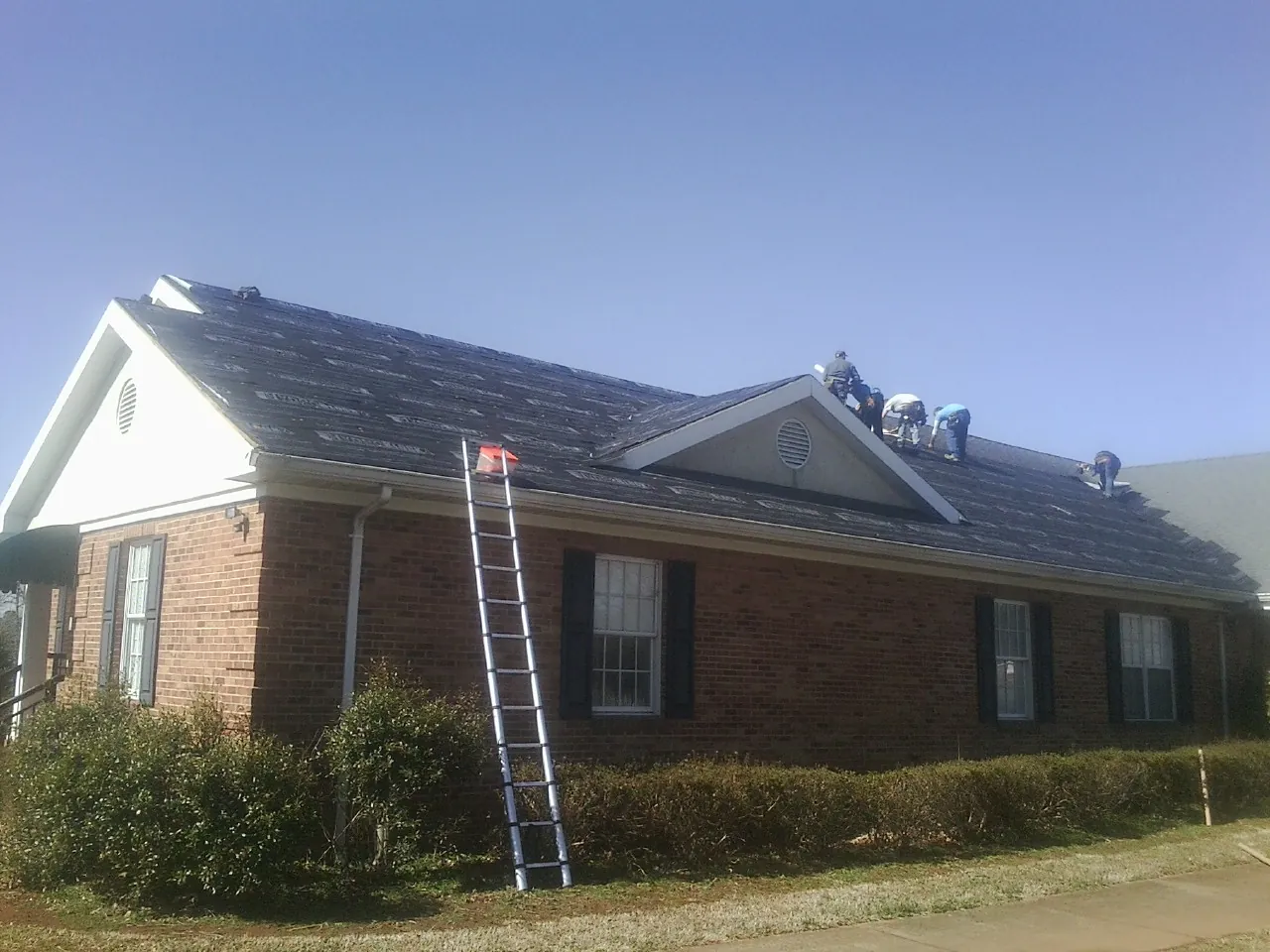 Crew tearing shingles off a brick ranch roof with a ladder set — Metal Roof Repair work by our crew in Bostwick