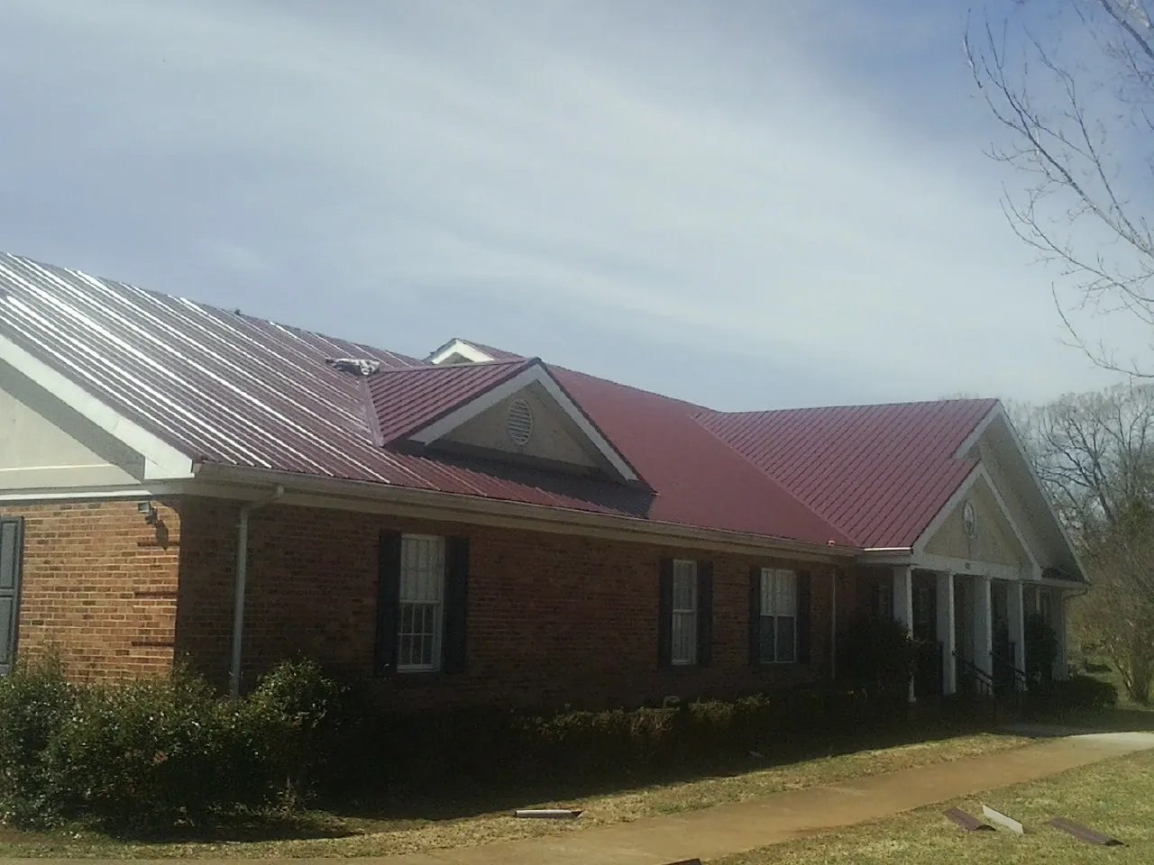 Red metal roof with gabled entries on a long brick building, from a Hail Damage Roof Repair job in Bostwick