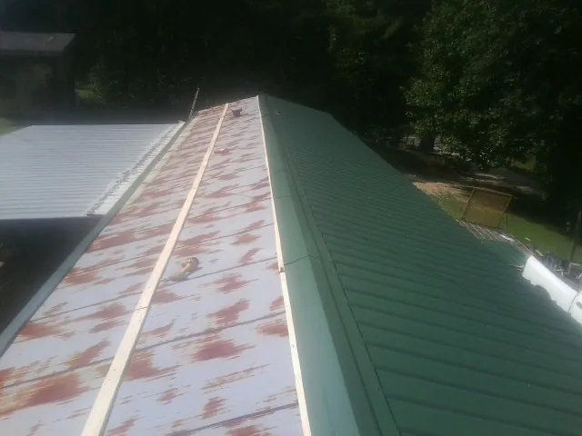 Old rusted panels beside newly installed green metal roofing — Wind Damage Roof Repair by Roofing Brothers in Bostwick