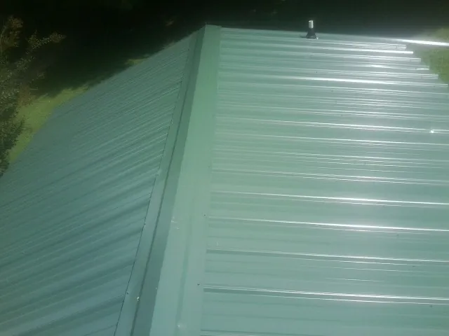 New green metal panels meeting at the ridge of a roof — Flat Roof Repair work by our crew in Bostwick