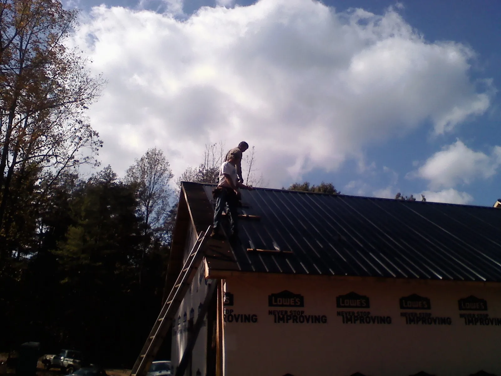 Roofer fastening dark metal panels high against a cloudy sky, from a Roof Inspection job in Bostwick