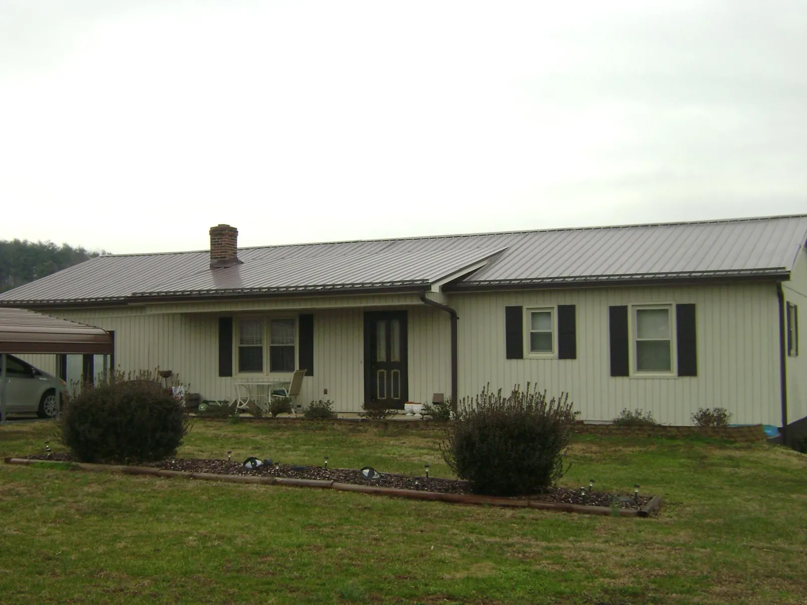 Brown metal roof on a cream sided ranch home with a brick chimney in Bostwick