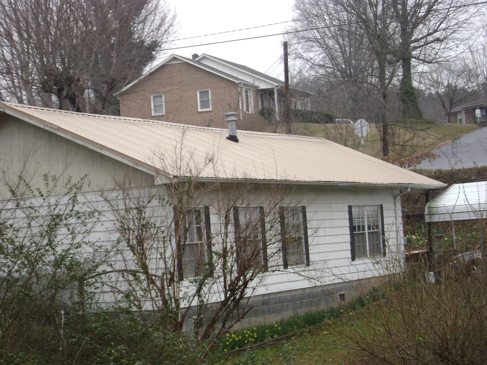 Tan metal roof on a white sided house set into a hillside — Commercial Roofing by Roofing Brothers in Bostwick
