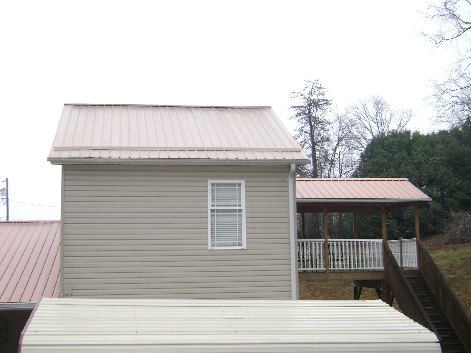 Tan metal roofs on a two story addition and attached porch, from a Roof Replacement job in Bostwick