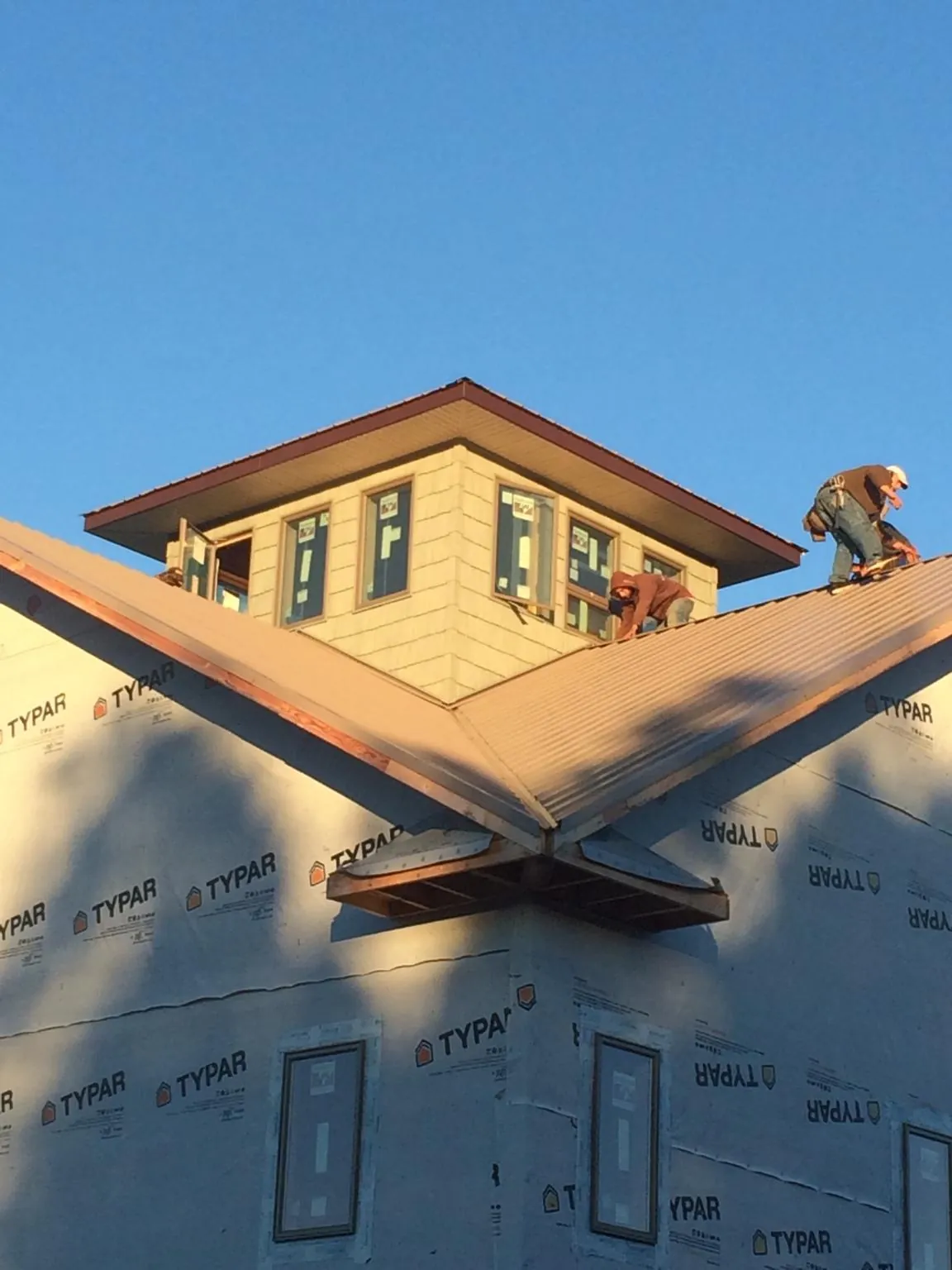 Roofers working around a rooftop cupola on a new metal roof at sunset — Roof Waterproofing in Bostwick by Roofing Brothers